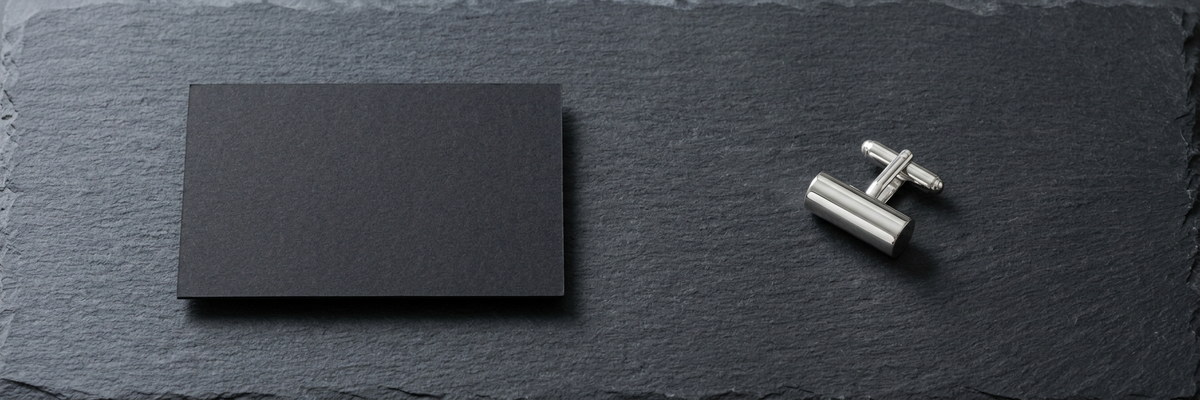 Polished silver cufflink and matte black business card on dark slate