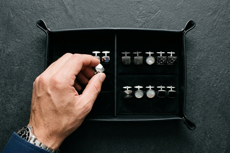 Man's hand selecting a silver cufflink from a curated display of classic styles